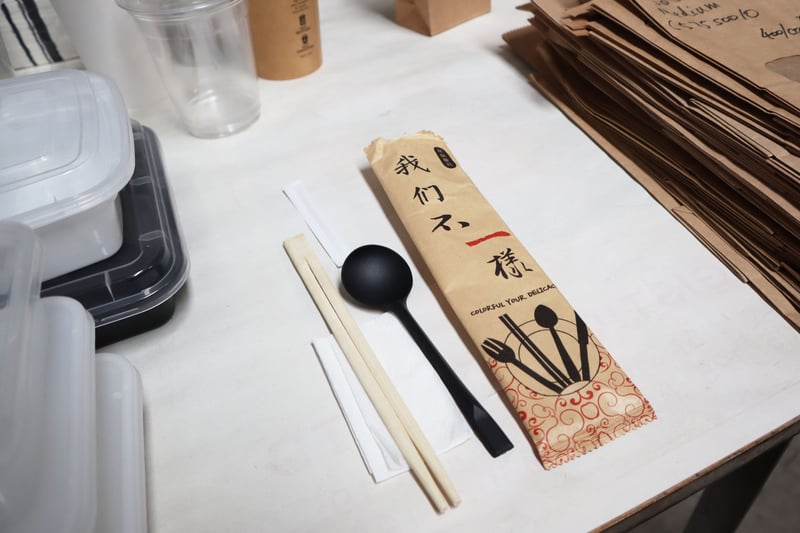 4 in 1 cutlery set which includes wooden chopsticks, a black plastic spoon, mini napkin and individually wrapped toothpick by FoodByUs Supplier, CP Blossom